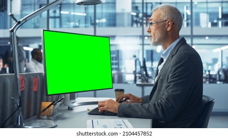 Diverse Modern Office: Senior Caucasian IT Technician Using Desktop Computer with Green Chroma Key Screen. Engineer Administrator Work on e-Commerce Development, Project Marketing, Big Data Analysis - Powered by Shutterstock