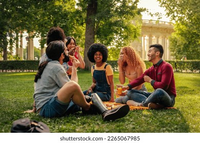 A diverse multicultural group of friends are having a picnic in the community park in the city - Powered by Shutterstock