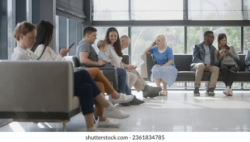 Diverse multicultural people sit on couches in clinic lobby area, wait for appointment with doctor or medical test results. Waiting area in medical center with modern design. Healthcare system.