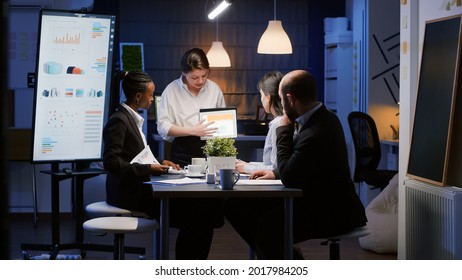 Diverse multi-ethnic businesspeople analyzing management graphs using tablet for company presentation working in office meeting room. Focused manager discussing corporate ideas in evening - Powered by Shutterstock