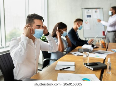 Diverse Multiethnic Colleagues Putting On Medical Masks During Corporate Meeting In Modern Office, International Business Team Following Coronavirus Prevention Measures At Workplace, Selective Focus - Shutterstock ID 2060158805