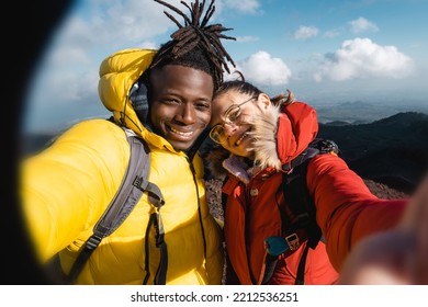 Diverse Multiethnic Couple Of Young Hikers Taking Selfie On The Peak Of The Mountain - Girlfriend And Boyfriend Having Fun, People Wanderlust And Technology Lifestyle Concept