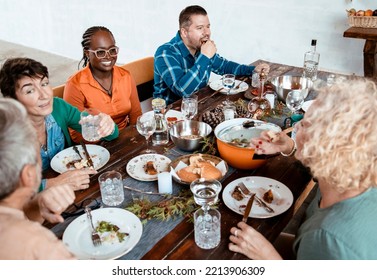 Diverse Multiethnic friends dining together in home patio, enjoying celebrate Holiday together with food and laugh. Family gathering around kitchen table on Thanksgiving day - Powered by Shutterstock