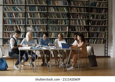 Diverse multiethnic group of young college students cooperating on graduation project in library, discussing research study, sitting at table with books, sharing learning tasks. Wide shot - Shutterstock ID 2111420609