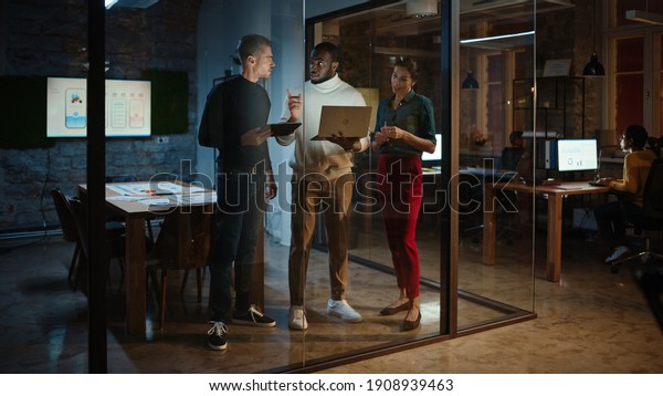 Diverse Multiethnic Team are Having a\
Conversation in a Meeting Room Behind Glass Walls in an Office.\
Black Creative Director Talks to Project Managers About the Work\
and Shows Brief on\
Laptop.