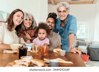 Diverse, multigenerational family gathers around the kitchen table, sharing a joyful moment - grandparents, parents, and a child smile warmly, reinforcing the bonds of family. - Powered by Shutterstock