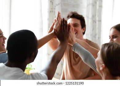 Diverse multiracial cheerful students giving high five greeting each other. Multi-ethnic millennial group of young people slapping palms sitting indoors. Gesture of celebration, friendship and unity