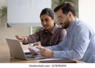 Diverse multiracial colleagues sit at desk look at laptop screen discuss company financial project together. Serious multiethnic coworkers work collaborate brainstorm using computer at office meeting. - Shutterstock ID 2178785993