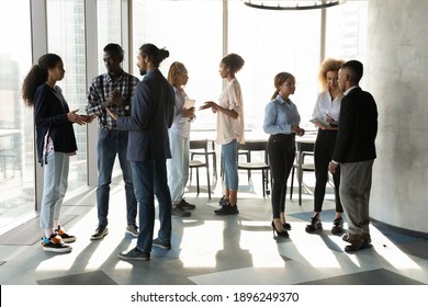 Diverse multiracial colleagues talk in groups discuss ideas at casual team meeting in office. Focused multiethnic businesspeople speak brainstorm cooperate at workplace. Teamwork concept. - Shutterstock ID 1896249370
