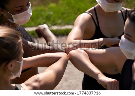 Diverse multiracial fit girls friends wear face masks give elbow bump. Sporty african, indian and caucasian young women group non-contact greeting together starting outdoor fitness training. Closeup.