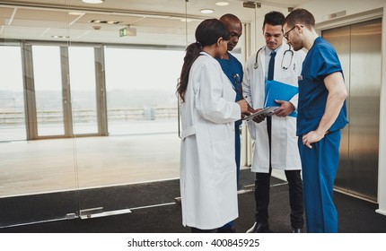 Diverse multiracial medical team consulting on a patient records standing in a foyer at a hospital grouped around a tablet computer