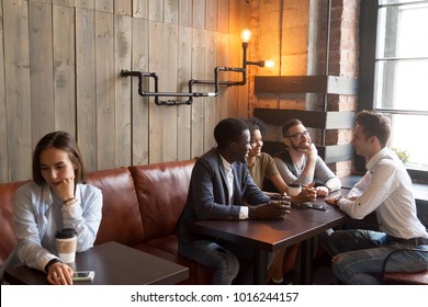 Diverse multiracial people hanging together in coffeehouse ignoring sad young girl sitting alone at cafe table, upset social outcast loner suffers from unfair attitude or discrimination among friends - Shutterstock ID 1016244157