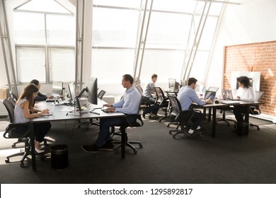 Diverse multiracial workers sitting at desk working in coworking space. Busy six businesspeople coworkers using computers typing chatting solving business matters in modern light contemporary office