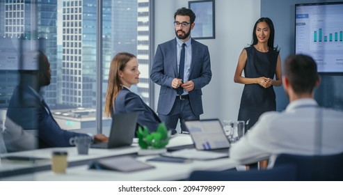 Diverse Office Conference Room Meeting: Team of Male Executive and Female Top Manager Present e-Commerce Startup Stock Market Growth Statistics to a Group of Investors. Wall TV with Infographics Data - Powered by Shutterstock