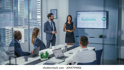 Diverse Office Conference Room Meeting: Male Executive And Asian Female Top Manager Present E-Commerce Fintech Startup Growth Statistics, Answers Questions Of Investors. Wall TV With Infographics Data