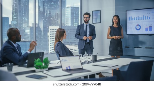 Diverse Office Conference Room Meeting: Male Executive And Asian Female Top Manager Present E-Commerce Fintech Startup Growth Statistics To A Group Of Investors. Wall TV With Infographics Data