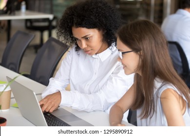 Diverse Office Workers Caucasian Woman Black Female Sitting At Desk Looking At Computer Discussing Working Moments. African American Employee Manager Shows Points On Pc Desktop Talking With Co-worker