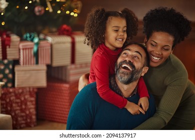 Diverse parents and their daughter sitting in front of Christmas tree in the living room and enjoying festive time together