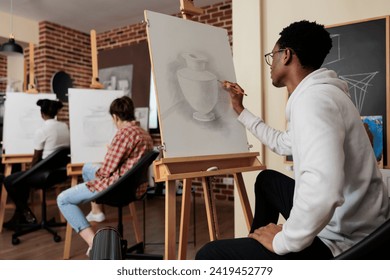 Diverse people engaged in arts activities. Young African American guy practicing sketching skills during art workshop, learning to draw in group, taking up drawing class, creating masterpiece - Powered by Shutterstock