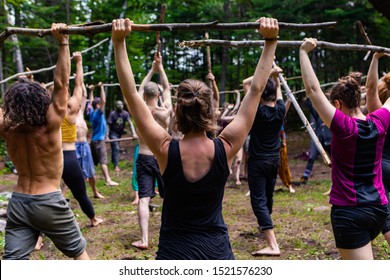 Diverse people enjoy spiritual gathering A mixed group of people are seen standing together in a forest clearing as they practice mindful tai chi exercises, holding sticks above their heads. - Powered by Shutterstock