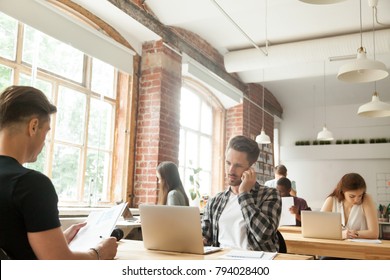 Diverse people focused on work in modern loft co-working space interior, businessman talking on phone while other businesspeople using laptops working with documents sitting at shared office desks - Powered by Shutterstock