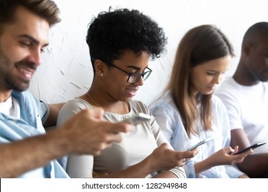 Diverse people guys and girls sitting together holding mobile phones, feel more comfortable chatting online than talking real life. Generation addicted to their smartphones modern technologies concept