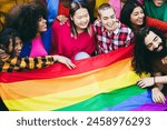 Diverse people having fun holding LGBT rainbow flag outdoor - Multiracial friends having fun together after gay pride event - Focus on center bald girl face