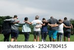 Diverse people hugging each other. Diverse group of men and women embrace each other at park. Unity and teamwork. Backside of friends standing in row huddle on green grass. Group of friends huddle