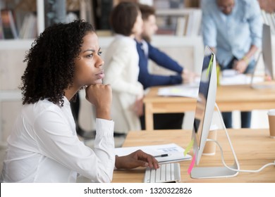 Diverse People In Office Area, Focus On Pensive African Employee Woman Sitting At Desk In Front Of Pc, Thinking Analyzing Market. Puzzled Biracial Worker Having Doubts Trying To Solve Business Problem