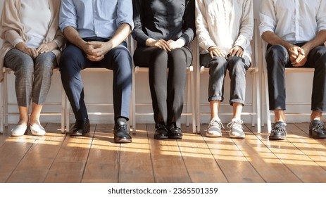 Diverse people seated on chairs in row waiting in queue job interview turn. Five unemployed unrecognizable applicants in corridor anticipating. Concept of recruiting agency, human resources, workforce - Powered by Shutterstock