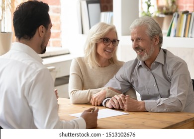 Diverse people sit at desk in office, male realtor make property offer for sale to elderly spouses old customers contract lie on table, buy new home, take bank loan or medical health insurance concept