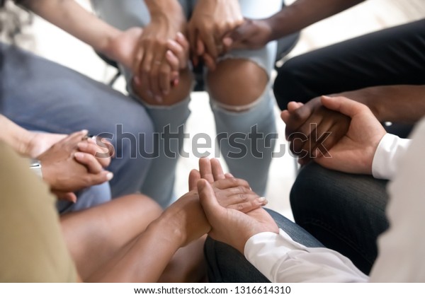 Diverse people sitting in circle holding hands at\
group therapy session, religious christian team pray together for\
recovery give psychological support, counseling training trust\
concept, close up