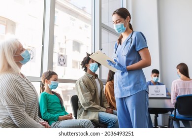 Diverse People Sitting In Line Waiting For Their Turn To Get Shots At The Hospital Vaccination Center. Nurse Talking With Multicultiral Patients In Queue For Antiviral Covid-19 Or Flu Vaccine