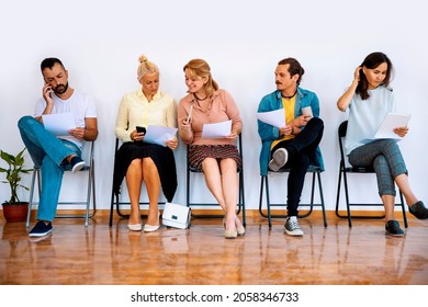 Diverse People Sitting On Chairs In A Row. Group Of Multiethnic People In Waiting Room With Paper Document In Hands