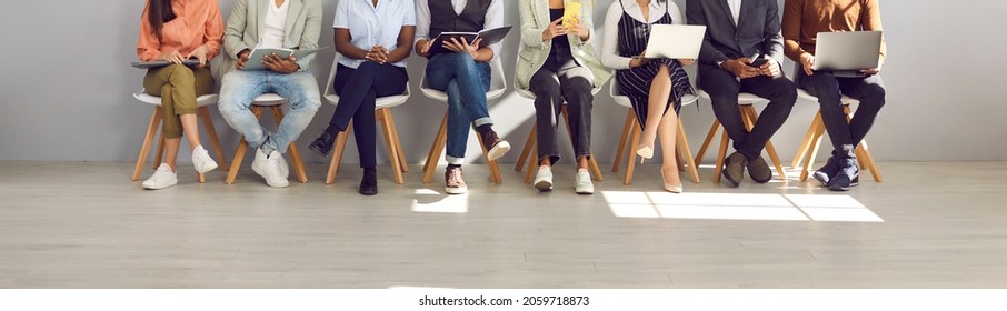 Diverse people in smart casual clothes holding paper documents, CVs, resumes, laptops and cellphones waiting in line for job interviews or business appointments in recruitment agency, legs low section - Powered by Shutterstock