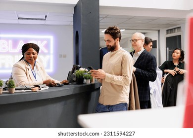 Diverse people standing in line with clothes in hands while shopping on Black friday at fashion store. Customers waiting for payment at cash register, buying clothing items at discounted prices - Powered by Shutterstock