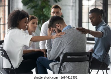 Diverse people supporting unhappy man at therapy session, touching shoulders, sitting in circle. Stressful businessman getting psychological help, trust and support, drug alcohol addiction treatment. - Shutterstock ID 1694416351
