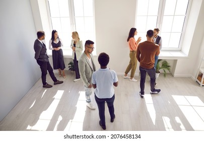 Diverse people talking in groups during a meeting. High angle shot of different young community members or company employees standing in a modern office room, discussing something, sharing opinions