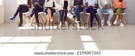 Diverse people waiting in line for appointment, job interview or work meeting. Group of male and female candidates sitting in corridor, reading, using different devices. Low section shot of human legs