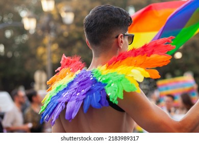 Diverse Person Walking At Pride Parade With Rainbow Flag Feathers As Symbol Of Pride Month. Queer Community March In The Street With Crowds. LGBTQIA March: VALENCIA, SPAIN - JUNE 25 2022