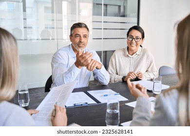 Diverse professional executive team working at meeting in office. Mid aged business man manager leader talking to board people consulting partners investors discussing project management in teamwork.