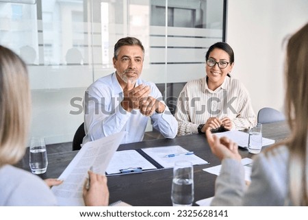 Diverse professional executive team working at meeting in office. Mid aged business man manager leader talking to board people consulting partners investors discussing project management in teamwork.