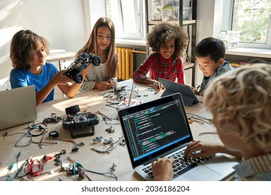 Diverse school children students build robotic cars using computers and coding. Happy multiethnic kids learning programming robot vehicles sitting at table at STEM education science engineering class. - Shutterstock ID 2036186204