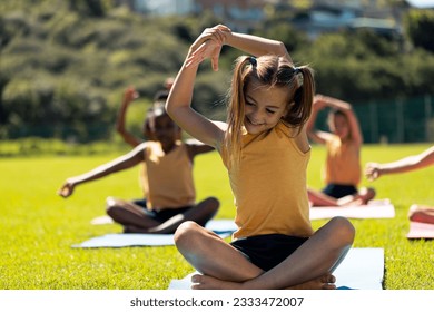 Diverse schoolgirls practicing yoga meditation on sunny elementary school sports field. School, health, wellbeing, childhood and education, unaltered. - Powered by Shutterstock