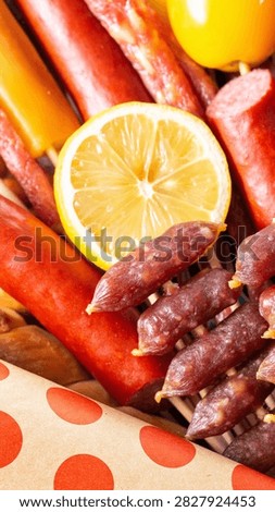 Diverse selection of processed meat products arranged artfully on wooden skewers, complemented by bright citrus fruit slice and decorative polka dot paper. Appetizing display of savory snacks.