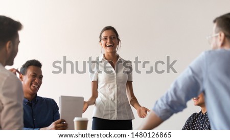Diverse seminar participants and coach have fun at corporate training, smiling businesswoman stand in front of multi-ethnic colleagues laughing discussing ideas, happy employees joke during briefing