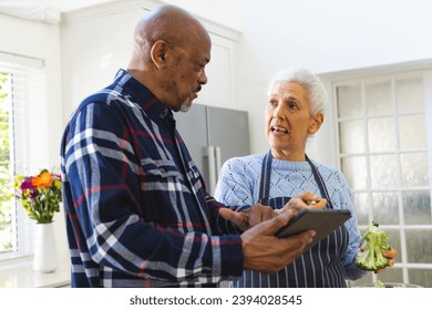 Diverse senior couple preparing healthy meal with vegetables using tablet in kitchen. Lifestyle, retirement, senior lifestyle, food, cooking, togetherness, recipe and domestic life, unaltered. - Powered by Shutterstock