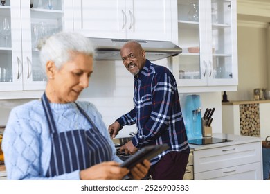 Diverse senior couple preparing meal using tablet in kitchen. Lifestyle, retirement, senior lifestyle, food, cooking, togetherness, communication, recipe and domestic life, unaltered. - Powered by Shutterstock