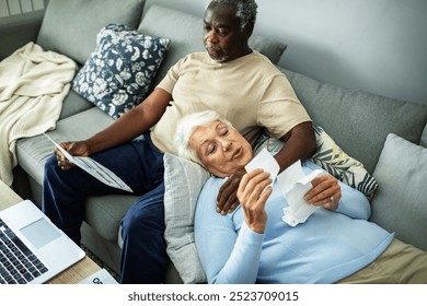 Diverse senior couple reading bills on the couch at home - Powered by Shutterstock