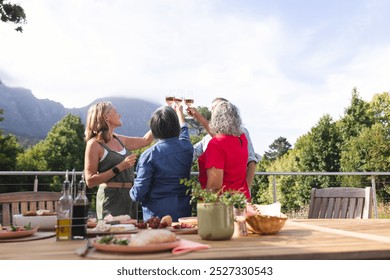 Diverse senior female friends toasting at outdoor table. Enjoying meal, laughing together with mountains in background, unaltered - Powered by Shutterstock